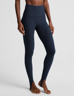 A model wearing high-waisted, full-length navy blue leggings against a light gray studio background.
