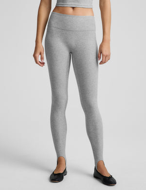 Woman wearing a gray tank top and gray stirrup leggings against a plain background. 