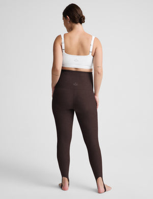 A woman shown from the back wearing high-waisted dark brown leggings and a white sports bra against a light gray studio background.