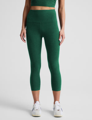 Woman wearing a green cropped tank and green capris against a plain background. 