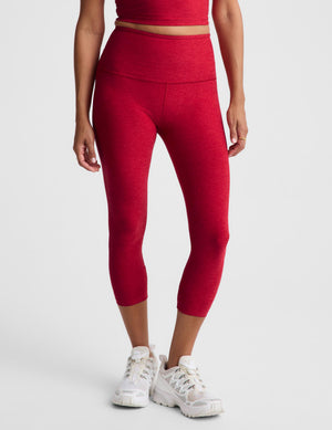 A model wearing high-waisted red capri leggings and white sneakers, shown from the waist down against a light gray studio background.