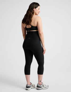 Woman wearing a bra and maternity capri leggings against a light gray background. 