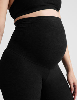 Woman wearing a bra and maternity capri leggings against a light gray background. 