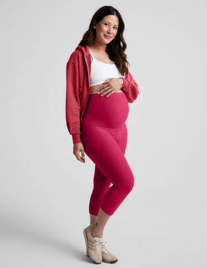 Woman wearing a red jacket, white bra, and red maternity capri leggings against a plain background. 