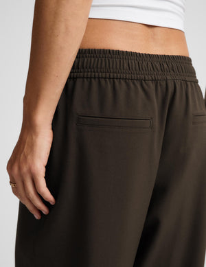 Close-up of a person wearing dark brown wide-leg sweatpants with an elastic waistband and side pocket, paired with a white cropped top against a light gray background.