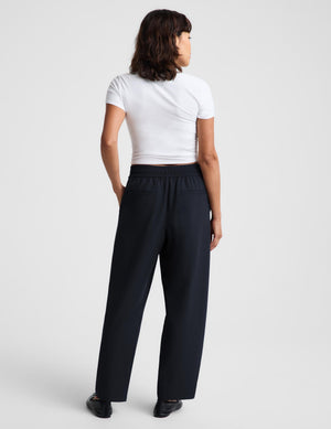 A woman modeling a white short-sleeve crop top and dark navy wide-leg trousers against a light gray studio background.