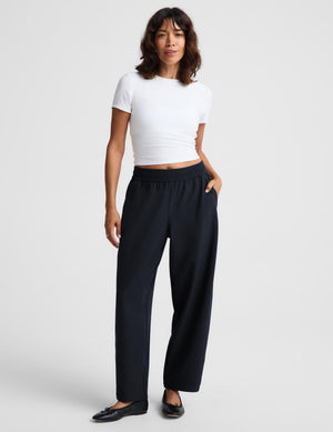 A woman modeling a white short-sleeve crop top and dark navy wide-leg trousers against a light gray studio background.