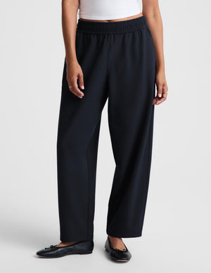 A woman modeling a white short-sleeve crop top and dark navy wide-leg trousers against a light gray studio background.