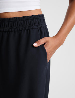 Close-up of a person wearing dark navy wide-leg athletic pants with an elastic waistband and side pocket, with one hand tucked into the pocket.