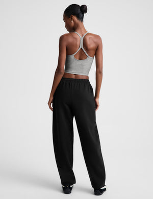 A woman shown from the back wearing a light gray cropped tank with crisscross straps and black wide-leg sweatpants, photographed against a clean light gray studio background.