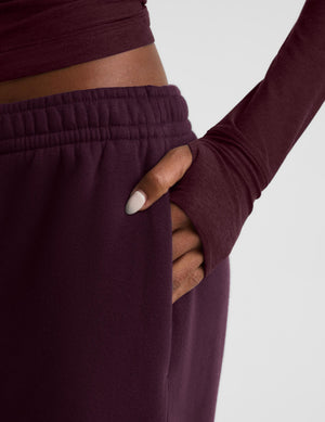 A model wearing a matching dark burgundy two-piece lounge set consisting of a long-sleeve top and wide-leg sweatpants, photographed against a neutral light gray studio background.