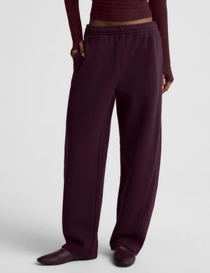 A model wearing a matching dark burgundy two-piece lounge set consisting of a long-sleeve top and wide-leg sweatpants, photographed against a neutral light gray studio background.