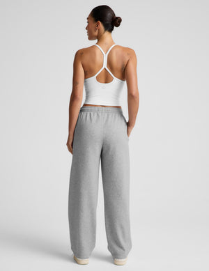 A woman shown from the back wearing a white sports bra with crisscross straps and light gray wide-leg sweatpants, photographed against a clean light gray studio background.