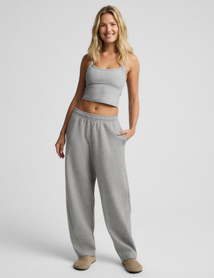 A woman modeling a light gray two-piece loungewear set consisting of a cropped tank top and matching sweatpants, standing against a light gray studio background.