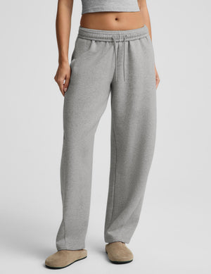 A person wearing light heather gray drawstring sweatpants with a cropped gray top and beige slippers, shown from the waist down against a light gray studio background.
