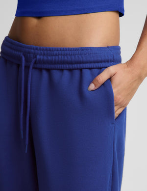 Close-up of a person wearing royal blue sweatpants with an elastic drawstring waistband and a matching blue cropped top, shown against a light gray studio background.