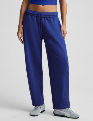 A model wearing royal blue wide-leg sweatpants with a drawstring waistband, paired with light gray sneakers, shown from the waist down against a light gray studio background.