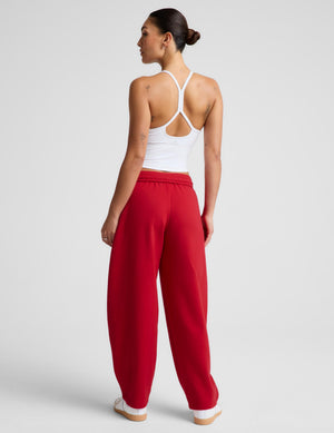 A woman shown from the back wearing bright red wide-leg sweatpants and a white strappy tank top, standing against a light gray studio background.