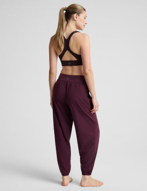 A woman modeling a black sports bra and burgundy jogger pants against a light gray studio background.