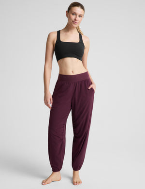 A woman modeling a black sports bra and burgundy jogger pants against a light gray studio background.