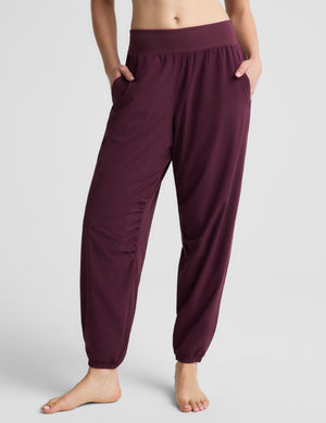 A woman modeling a black sports bra and burgundy jogger pants against a light gray studio background.