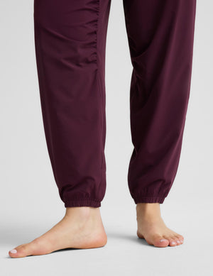 A woman modeling a black sports bra and burgundy jogger pants against a light gray studio background.