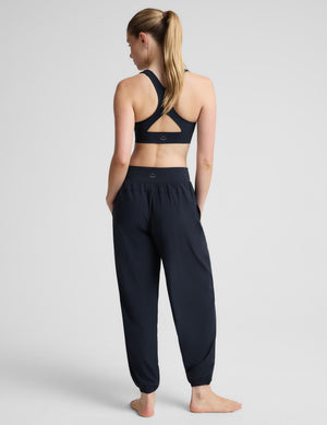 A woman modeling a matching dark navy activewear set consisting of a square-neck sports bra and high-waisted, relaxed-fit jogger pants with side pockets, shot against a light gray studio background.