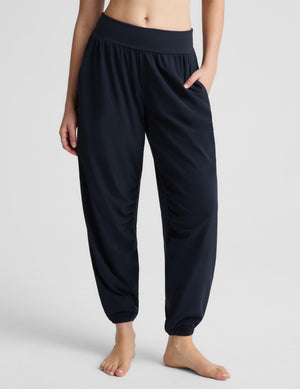 A woman modeling a matching dark navy activewear set consisting of a square-neck sports bra and high-waisted, relaxed-fit jogger pants with side pockets, shot against a light gray studio background.