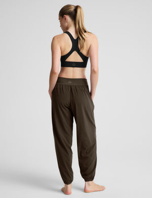 A woman modeling dark green jogger-style pants with a black sports bra against a light gray studio background.