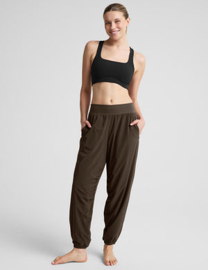 A woman modeling dark green jogger-style pants with a black sports bra against a light gray studio background.