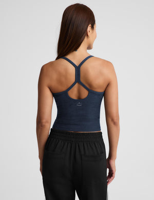 A woman modeling a dark navy blue camisole tank top paired with black track pants, photographed against a solid light gray background.