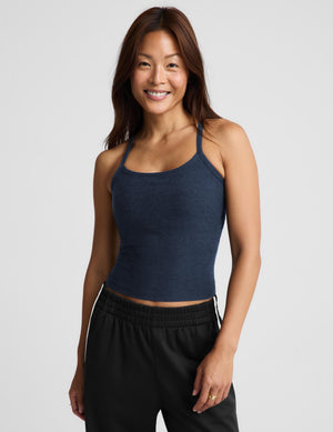 A woman modeling a dark navy blue camisole tank top paired with black track pants, photographed against a solid light gray background.
