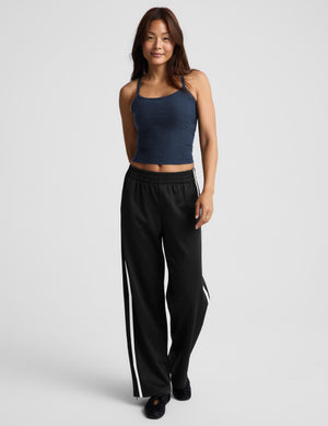 A woman modeling a dark navy blue camisole tank top paired with black track pants, photographed against a solid light gray background.