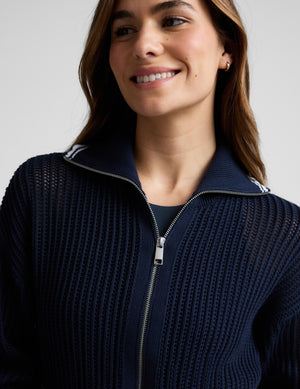 Woman wearing a blue zip-up sweater and skirt against a plain background. 