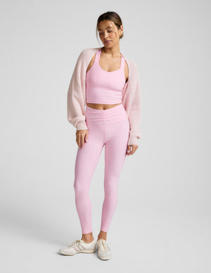 Woman wearing a pink shrug over a matching pink athletic set. 