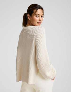 Woman wearing a beige hi lo sweater against a light gray background. 