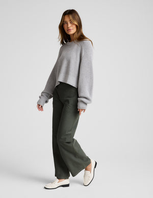 Woman wearing a gray sweater and green pants on a white background. 