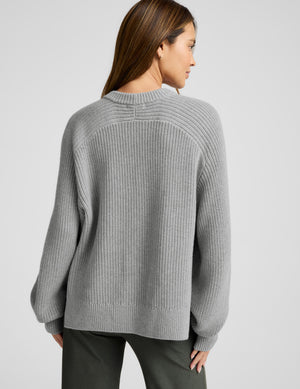 Woman wearing a gray sweater on a plain background. 