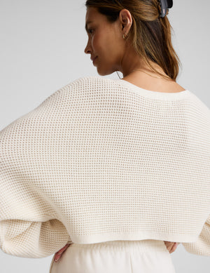 Woman wearing a white textured sweater against a plain background. 