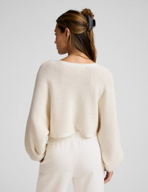 Woman wearing a cream-colored knit sweater and pants against a plain background. 