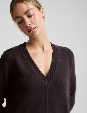 Woman wearing a brown v-neck long length sweater against a plain background. 