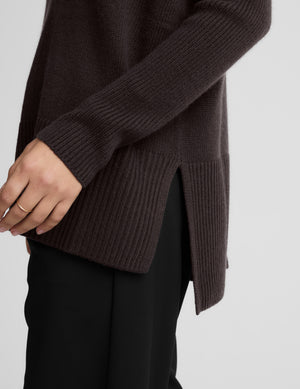 Woman wearing a brown v-neck long length sweater against a plain background. 