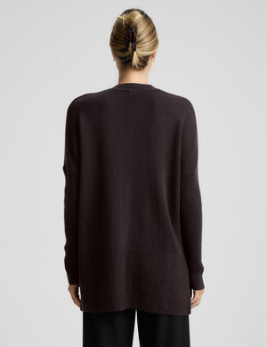 Woman wearing a brown v-neck long length sweater against a plain background. 