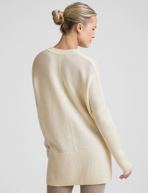 woman wearing a cream-colored v-neck sweater against a plain background. 