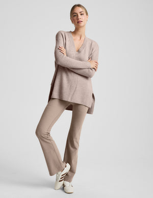 Woman wearing a beige v-neck sweater against a plain background. 