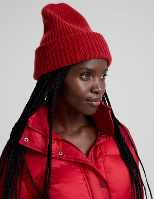 woman wearing a red ribbed beanie and puffer jacket against a plain background. 