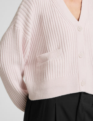 Woman wearing a light pink button-up cardigan and black pants against a plain background. 