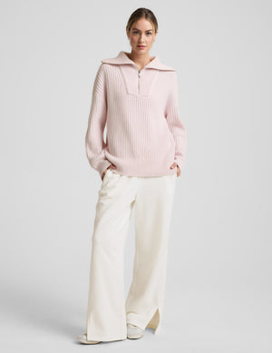 Woman wearing a light pink sweater with a zipper on a plain background. 