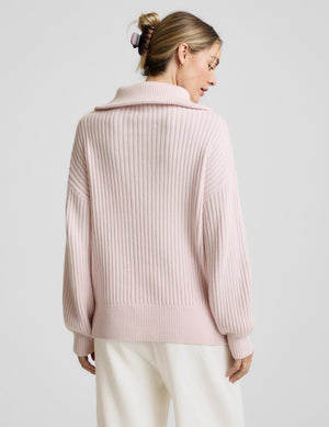 Woman wearing a light pink sweater with a zipper on a plain background. 