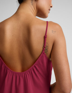 Woman wearing a magenta cupro mini dress and brown sandals against a plain background. 
